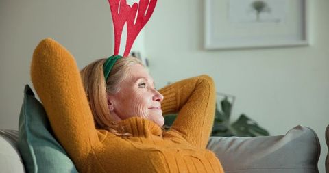 Senior woman relaxing on sofa in festive attire with antler headband