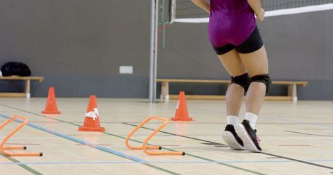 Asian volleyball player jumping through agility hurdles on indoor court wearing knee pads