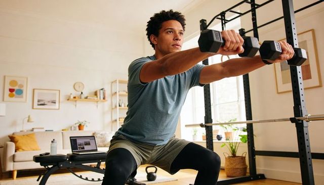 Man lifting dumbbells during home strength workout on bench, squat rack, natural light