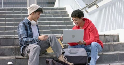 Male Students Collaborating on Laptop and Papers on Outdoor Urban Steps