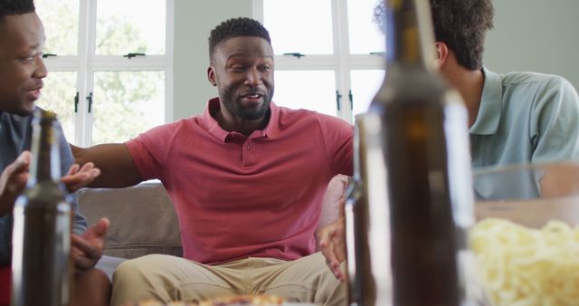 Men are engaging in a lively conversation while enjoying beers in a relaxed home environment. Suitable for themes related to friendship, leisure, socializing, and weekend activities.