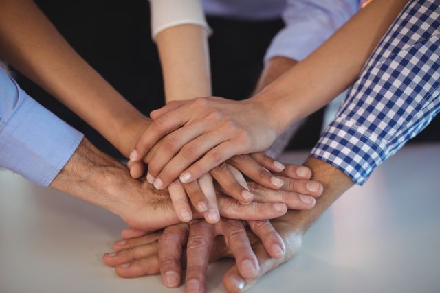 This image captures business colleagues stacking hands on a desk, symbolizing teamwork and unity in a corporate environment. Perfect for illustrating concepts like collaboration, team building, partnership, and collective effort in corporate presentations, marketing materials, and motivational posters.