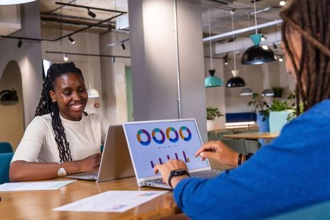 Smiling coworkers collaborating and pointing at laptop charts in modern workspace