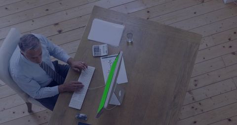 Overhead executive working at wooden desk typing on white keyboard with calculator and papers