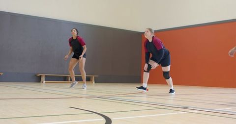 Female volleyball players in ready defensive stance on indoor court wearing matching jerseys
