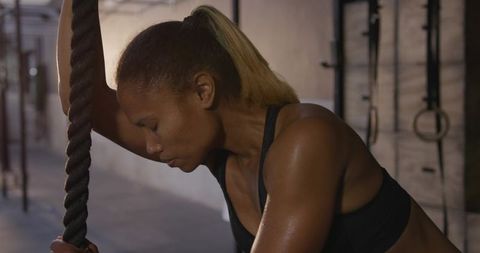 Determined african american woman leaning on rope at gym