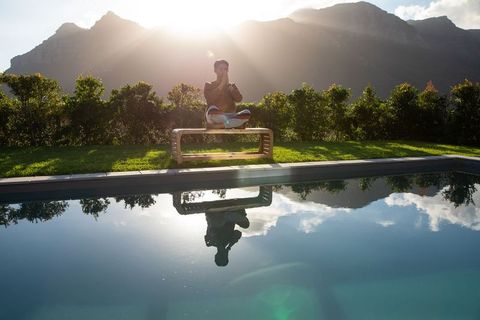 Asian man meditating cross-legged on curved bench by pool at sunrise with mountain reflection