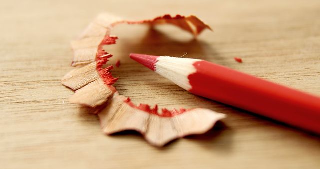 A sharpened red pencil lies next to its shavings on a wooden surface, with copy space. It suggests a moment of creativity, preparation for writing, drawing, or the beginning of an artistic project.