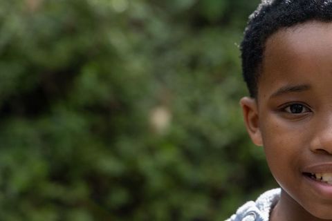 African american boy smiling close-up portrait with green bokeh background and copy space