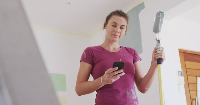 Woman Holding Paint Roller Checking Phone During Home Renovation - Download Free Stock Images Pikwizard.com