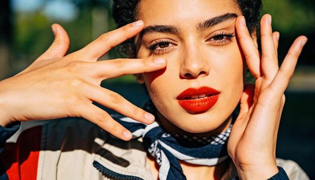 Sunlit closeup portrait of woman posing with hands framing face wearing red lipstick scarf