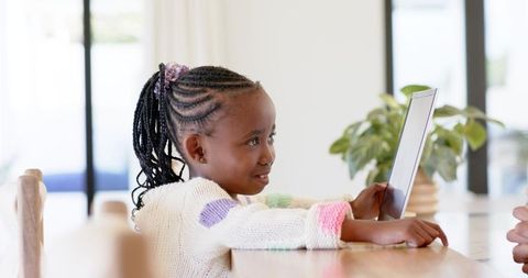 African american girl using tablet at dining table smiling during home learning and play