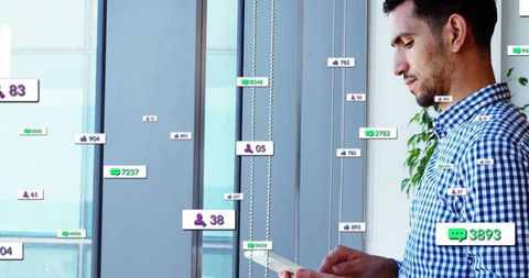 Businessman checking tablet with floating social media notifications in modern glass office