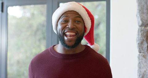 African american man wearing santa hat grinning in cozy holiday home portrait