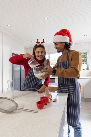 Couple baking together wearing festive hats and striped aprons in modern kitchen
