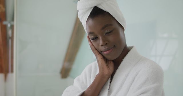 Portrait of smiling african american attractive woman wearing robe and turban in bathroom. beauty, pampering, home spa and wellbeing concept.