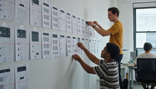 Design team aligning app wireframes on wall for ux planning, collaboration and testing