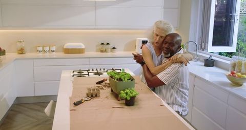 Senior couple embracing while planting herbs in modern kitchen