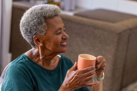Senior woman savoring steaming mug of coffee while smiling in cozy living room
