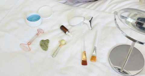 Skincare tools arranged on white towel showcasing jade roller rose quartz gua sha serums