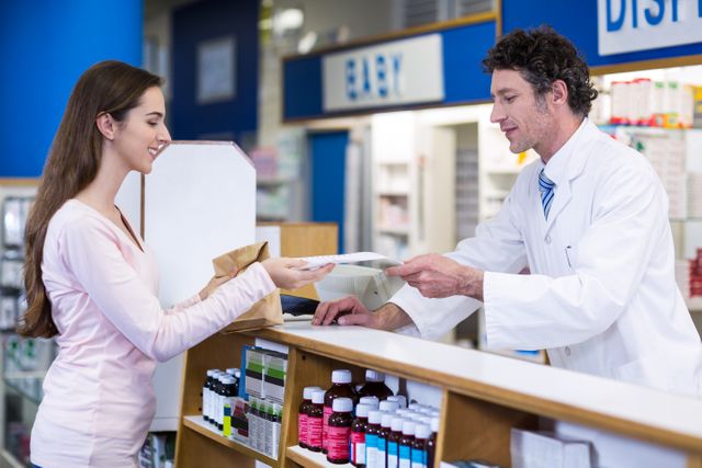 Pharmacist giving medicine package to customer at counter in pharmacy