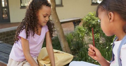 African american girls studying together on schoolyard bench with backpack and notebook