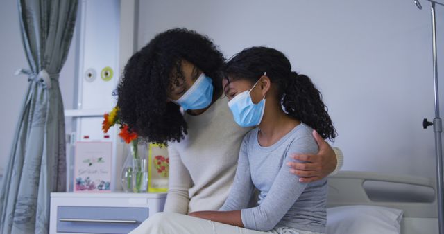 African american mother wearing face mask taking and comforting her daughter at hospital. medical healthcare during coronavirus covid 19 pandemic concept