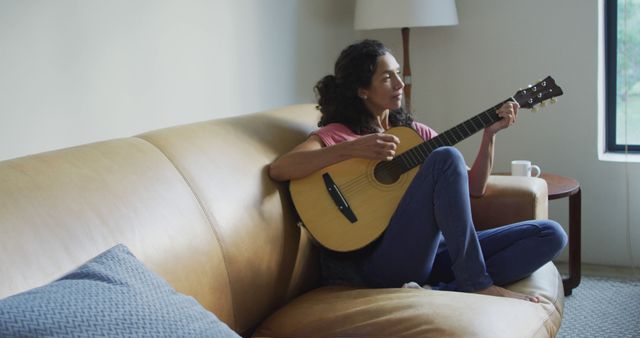Happy biracial woman sitting on the sofa playing with guitar - Download Free Stock Photos Pikwizard.com