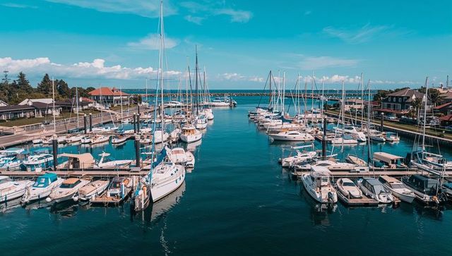 Panoramic marina channel featuring docked sailboats and motorboats with water reflections