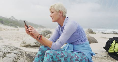 Senior Woman Trekker Resting on Beach Checking Smartphone - Download Free Stock Images Pikwizard.com