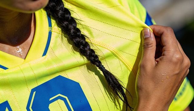 Female soccer player pulling neon jersey collar after sprinting, sweat glinting on number 10