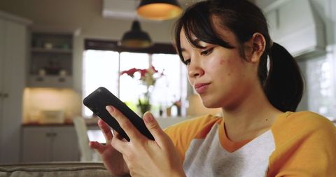 Asian woman engaged with smartphone in cozy home interior