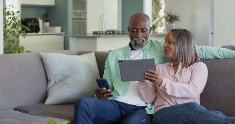 Senior couple using tablet and smartphone on modern sofa in open-concept living room