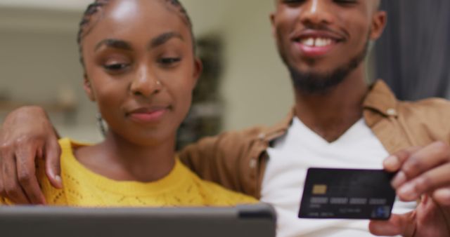 Happy african american couple sitting on sofa and making online shopping. Lifestyle, relationship, shopping and spending free time together concept.