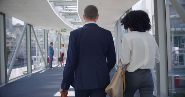 Business professionals walking through office corridor with cityscape views. Colleagues in conversation ahead. Ideal for corporate, teamwork, business meeting, office lifestyle visuals.