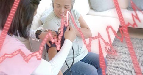 Caregiver measuring blood pressure for senior woman at home with health data overlay