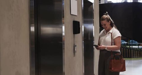 Professional at Elevator Door Checking Smartphone in Modern Office Lobby