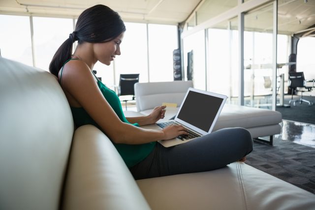 Side view of young businesswoman using laptop on sofa at office