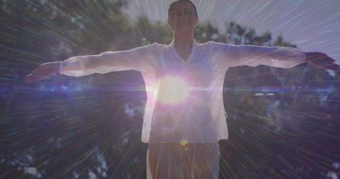 Woman standing arms outstretched in sunlit forest embracing radiant sun flare