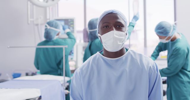 Surgeon wearing scrub suit and mask in a bright, modern operating room while medical team works in background. Suitable for illustrating concepts of healthcare, surgery, medical professionals, teamwork, and hospital environment.