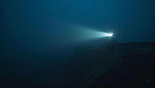 Mysterious Lighthouse Beacon Cuts Through Foggy Night on Coastal Cliff