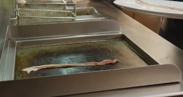 Chef laying bacon on a hot grill in a bustling restaurant kitchen. Scene captures essence of culinary arts and professional food preparation. Ideal for use in content related to restaurant operations, culinary schools, cooking tutorials, food industry articles, and professional chef profiles.