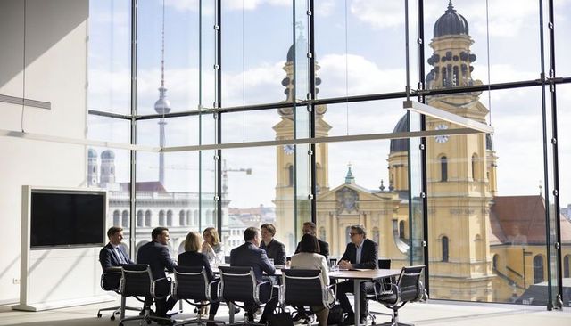 Executives discussing strategy in sunlit glass conference room with cathedral skyline view