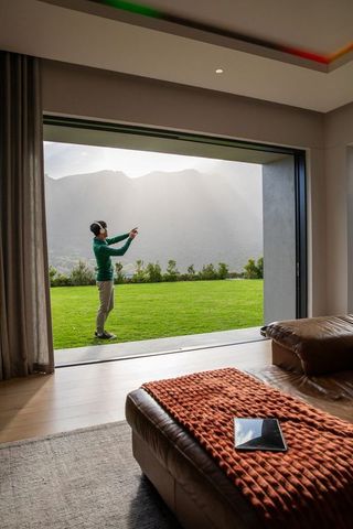 Asian man listening with headphones on lawn holding smartphone overlooking misty mountains