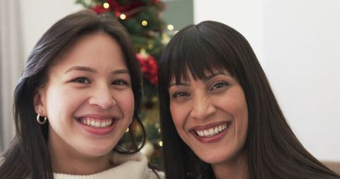 Happy Mother and Daughter Smiling in Front of Christmas Tree