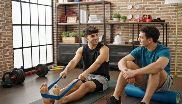 Friends training together stretching with resistance band in bright brick home gym