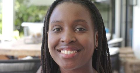Smiling black woman with dreadlocks on sunlit veranda showing warm confident smile
