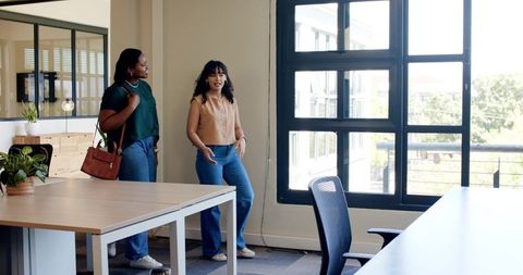 Two coworkers touring modern open-plan office discussing layout by sunlit window