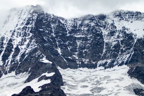 Jagged snow-covered mountain face with glacial cirque, crevasses and low clouds