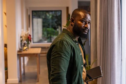 African American man standing by window holding tablet in modern minimalist home interior